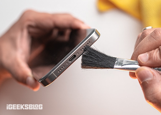 Cleaning the charging port of an iPhone with a soft-bristled brush.