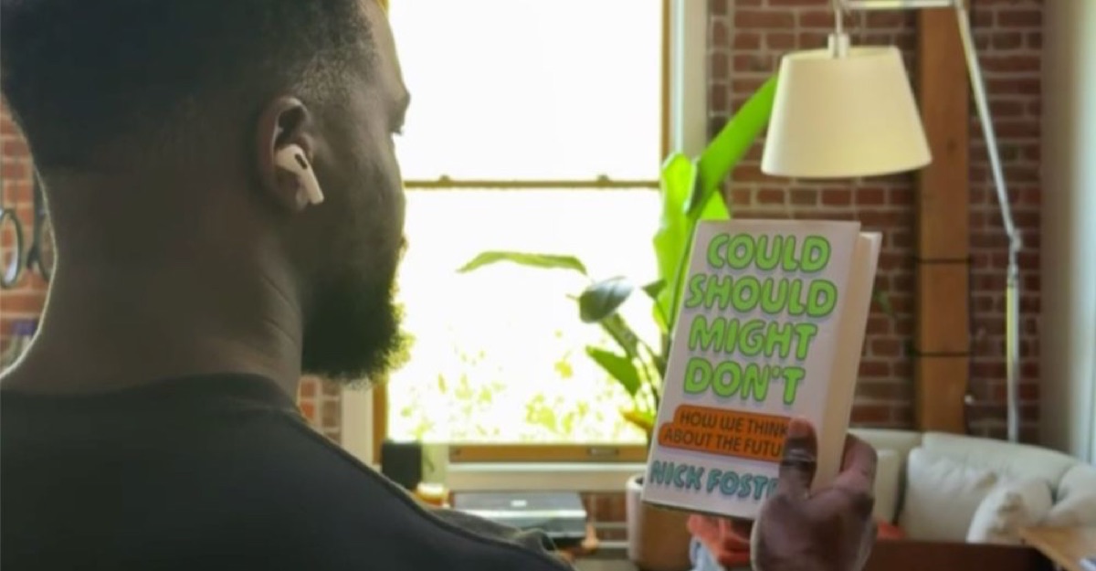 Still from Apple's demo video showing a person wearing camera-equipped AirPods holding up a book for Visual Intelligence