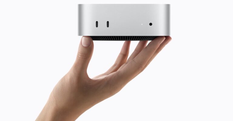 A hand holds the silver Mac mini and shows its front USB-C ports and headphone jack
