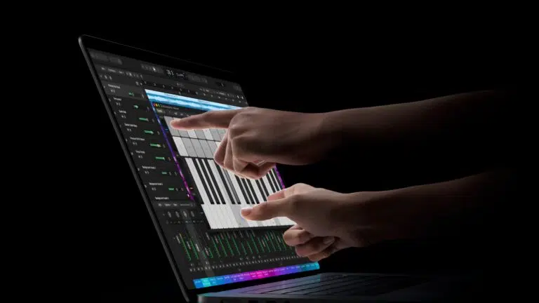 Hands type on a laptop displaying a digital audio workstation with multiple tracks and a piano roll in a dark studio setting