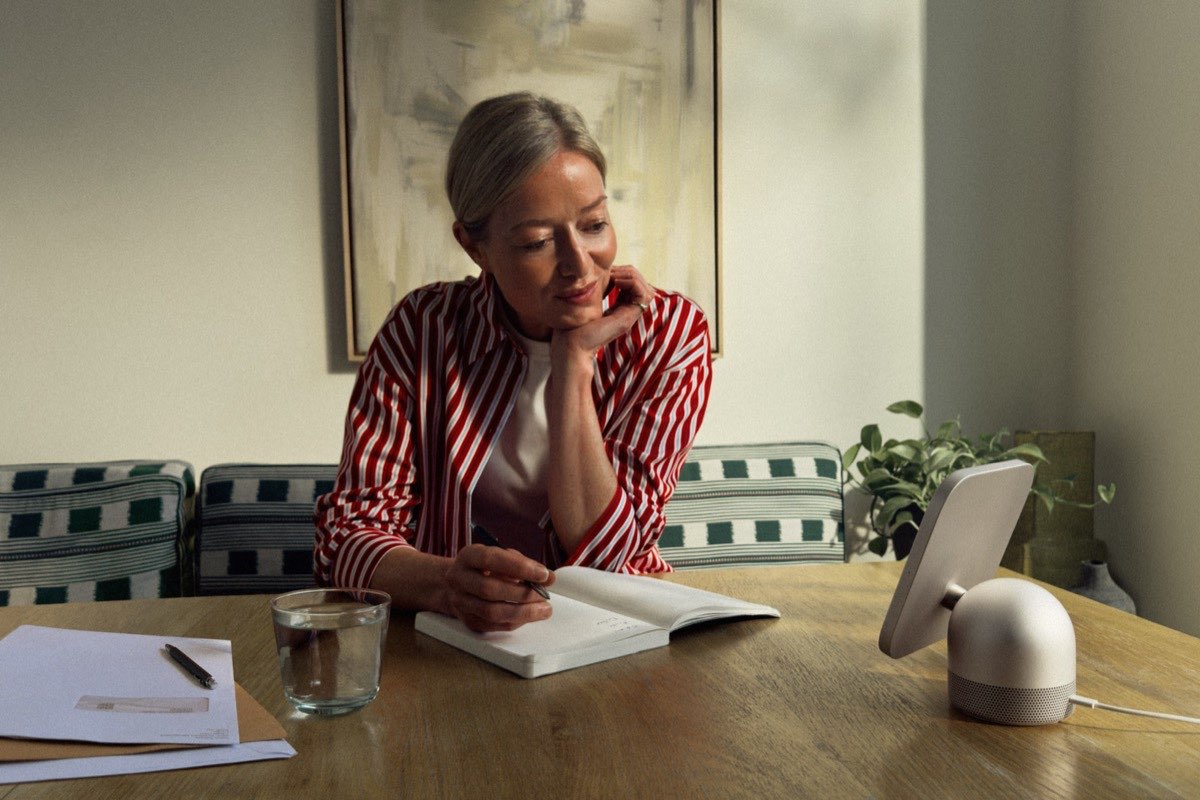 A woman writing in a notebook at a dining table beside a HomeView tabletop display