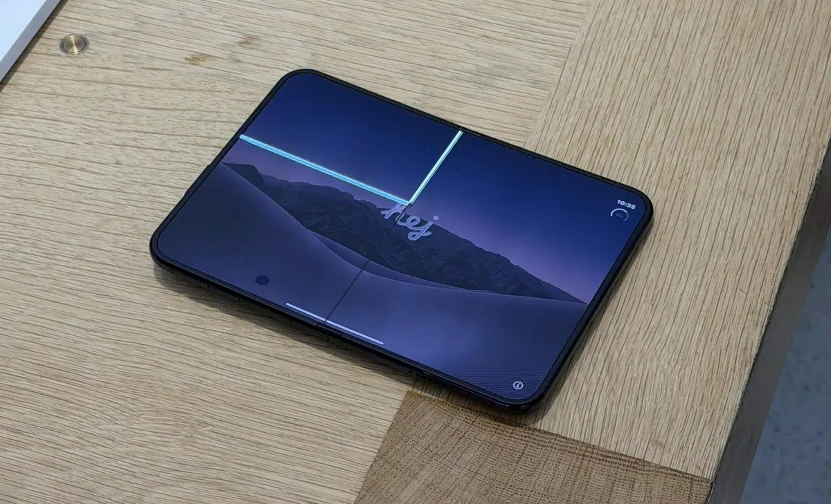 iPhone Duo cracked screen or white line? Here’s what to do Black smartphone lying screen-up on a light wood desk, displaying a purple mountain twilight wallpaper.