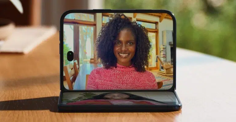 An open iPhone Duo on a wooden table, showing a smiling woman on a FaceTime call on its inner screen