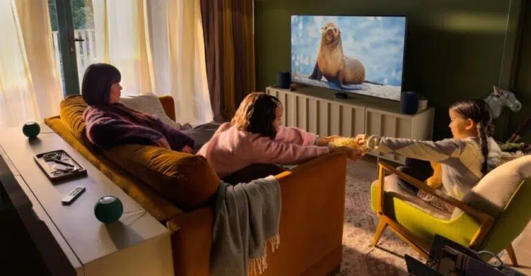 A warm living room with a family watching a nature documentary on a TV, with HomePod mini speakers around the screen