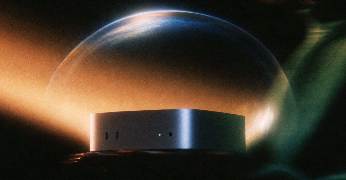Silver Mac mini in front of a glowing planet-like backdrop on a dark background