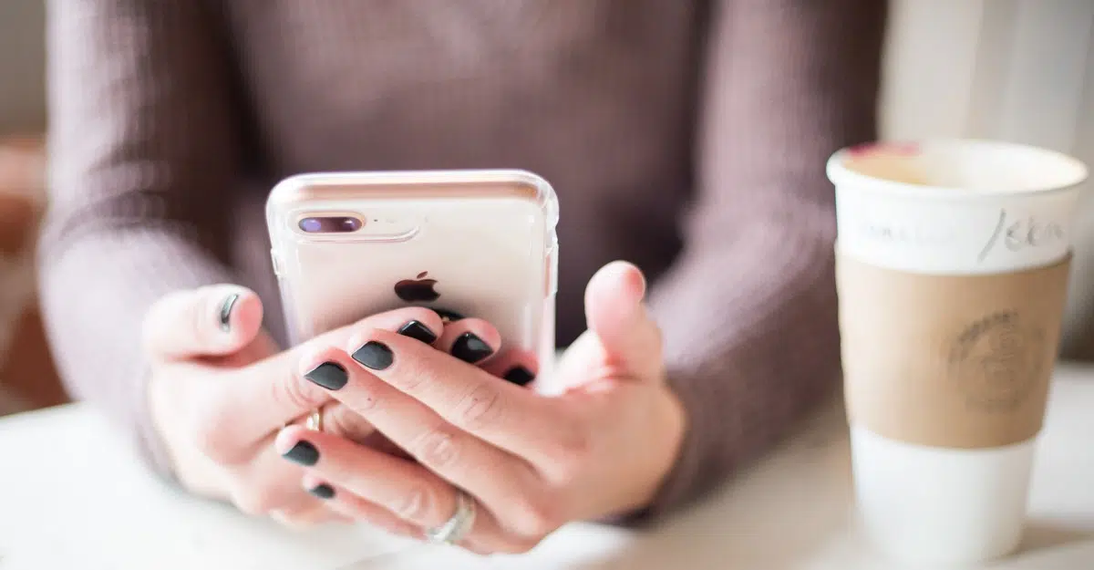 Woman holding an iPhone in a clear case, with a coffee cup on the table